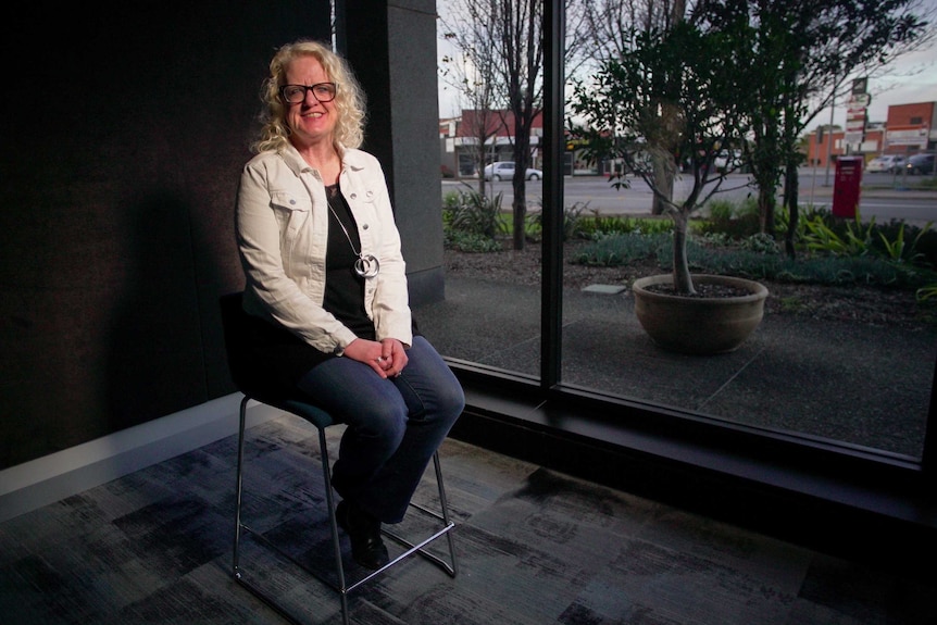 Elizabeth Beales sitting on a chair in front of a glass window