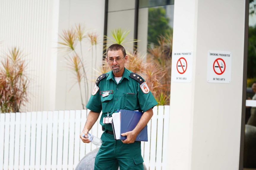Craig Garraway in a green ambulance uniform carries a blue clipboard leaving court.