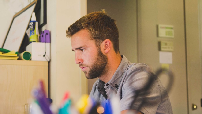 A young man sits at a desk.