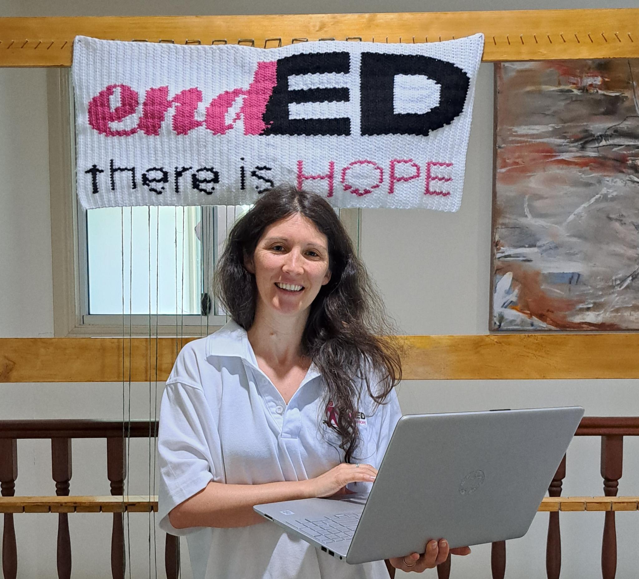 Laura Chamberlain smiles holding a laptop with endED signage in the background.