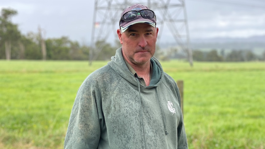 Andrew is standing in a paddock on his property in front of a transmission tower