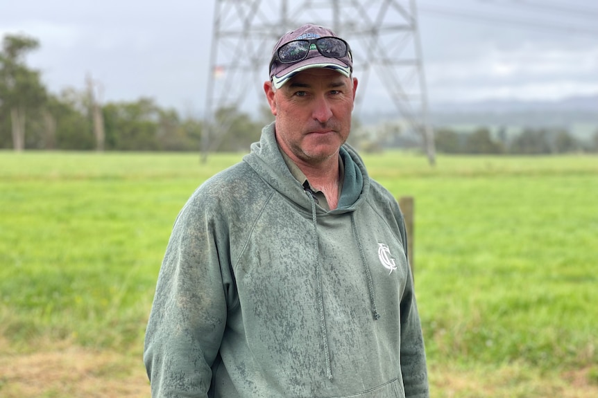 Andrew is standing in a paddock on his property in front of a transmission tower