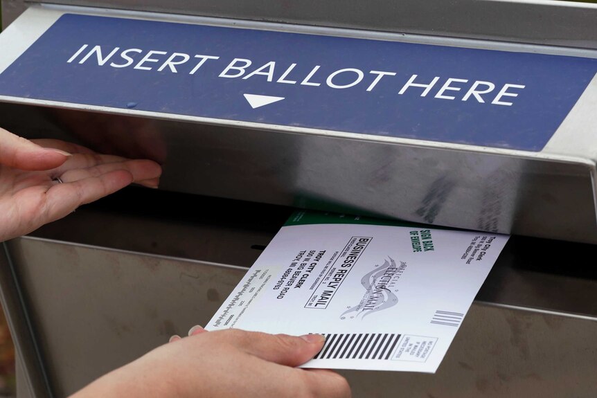 A voter inserts her absentee voter ballot into a drop box.