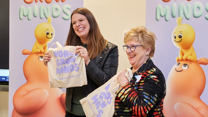 Two women smiling and holding a gift bag with a campaign slogan across it (words grow minds).