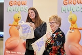 Two women smiling and holding a gift bag with a campaign slogan across it (words grow minds).