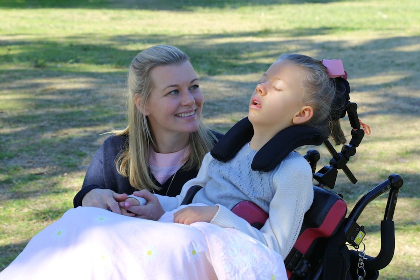 A woman smiles at a young girl in a wheelchair