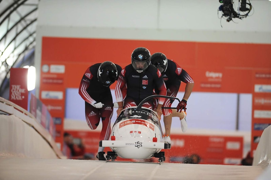 A team of four bobsled pilots about to jump into their sled.