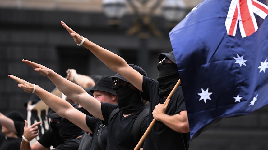 People dressed in black perform a Nazi salute in a line, one of them holding an Australian flag in their non-saluting hand.