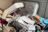 一所房子里的垃圾堆，包括旧床垫、自行车、箱子和瓶子。