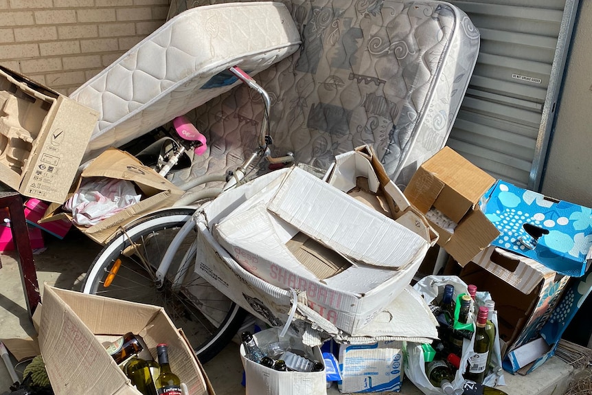 Pile of rubbish at a house, including old mattresses, bikes, boxes and bottles. 