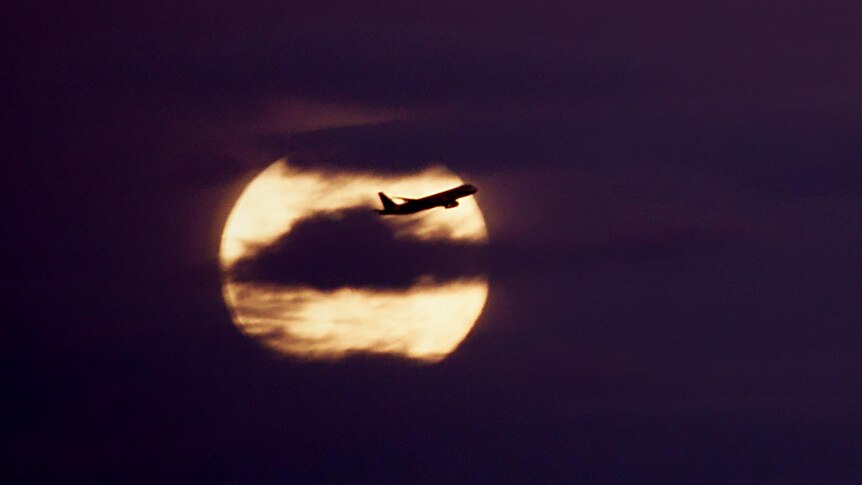 A passenger jet is silhouetted against the blue moon.