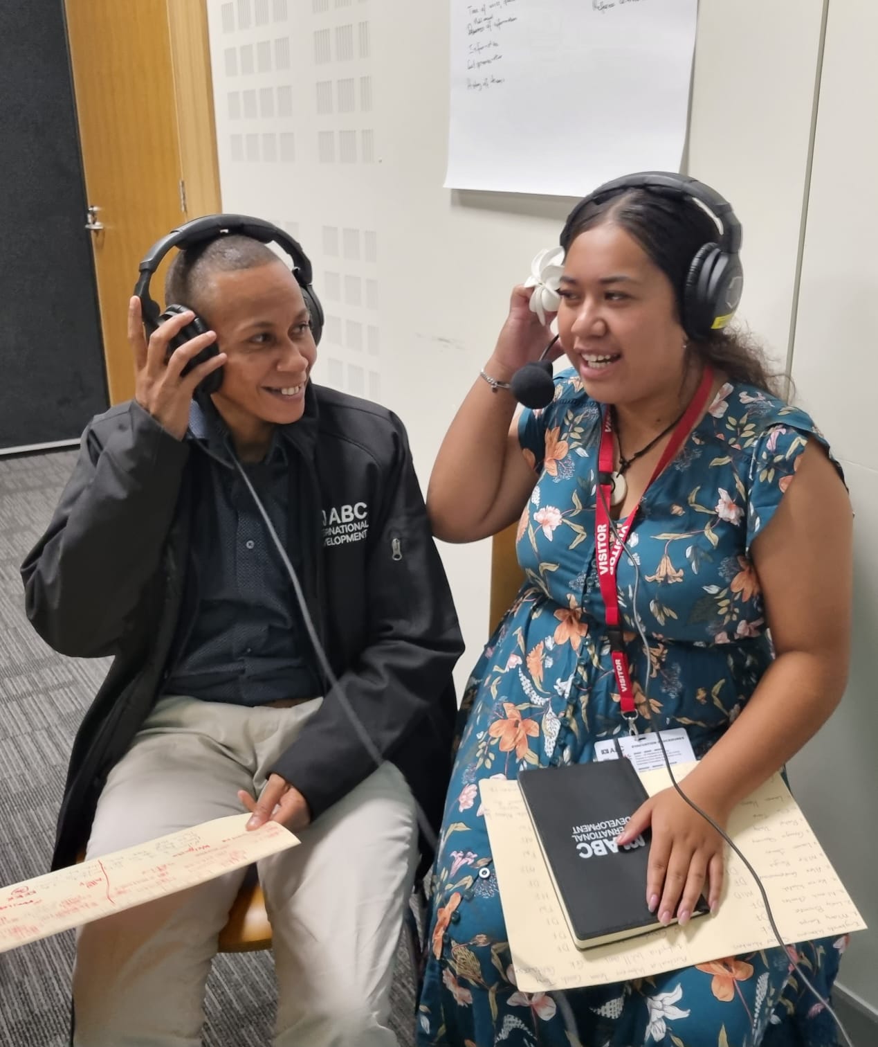 Two women wearing headsets with microphones attached looking at each other as though in conversation.