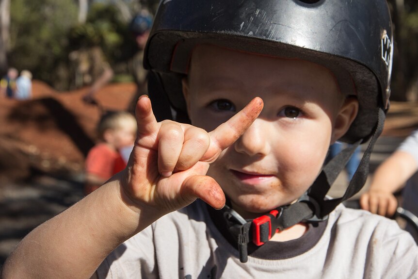 A young rider grins at the camera holding out his fingers in a rock n roll horn shape