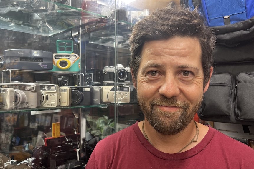 A man stands in a shop next to shelves of cameras