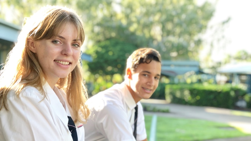 Girl and boy teenagers in formal uniform looking relaxed in school grounds.