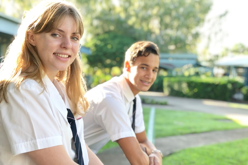 Girl and boy teenagers in formal uniform looking relaxed in school grounds.