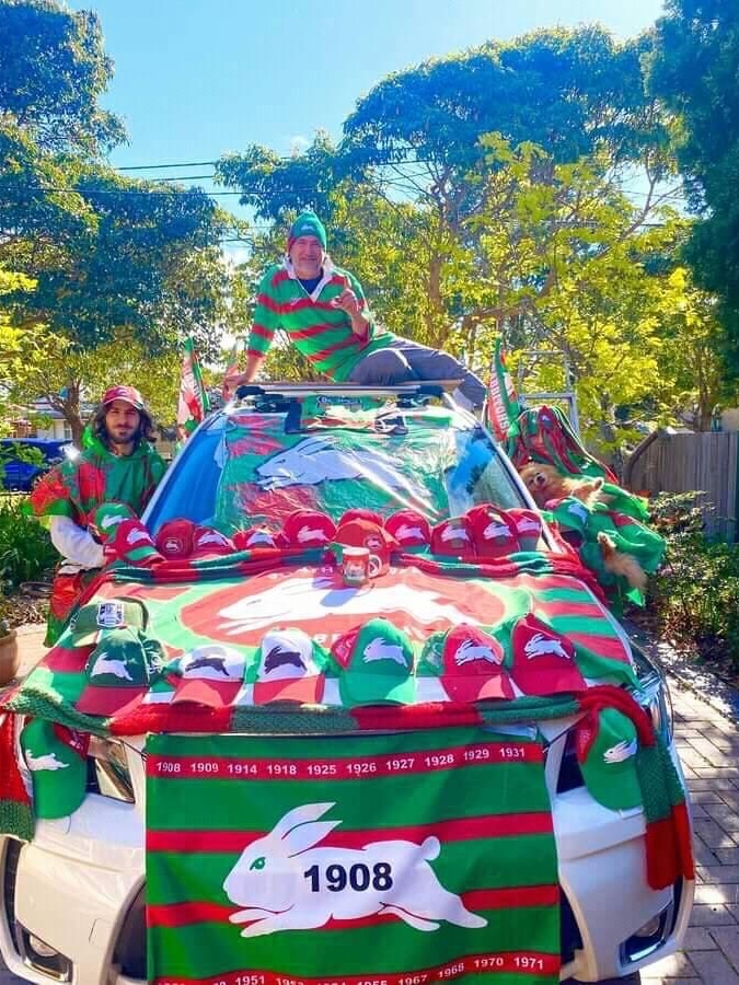 A man sits on top of his car, decorated in South Sydney paraphernalia 