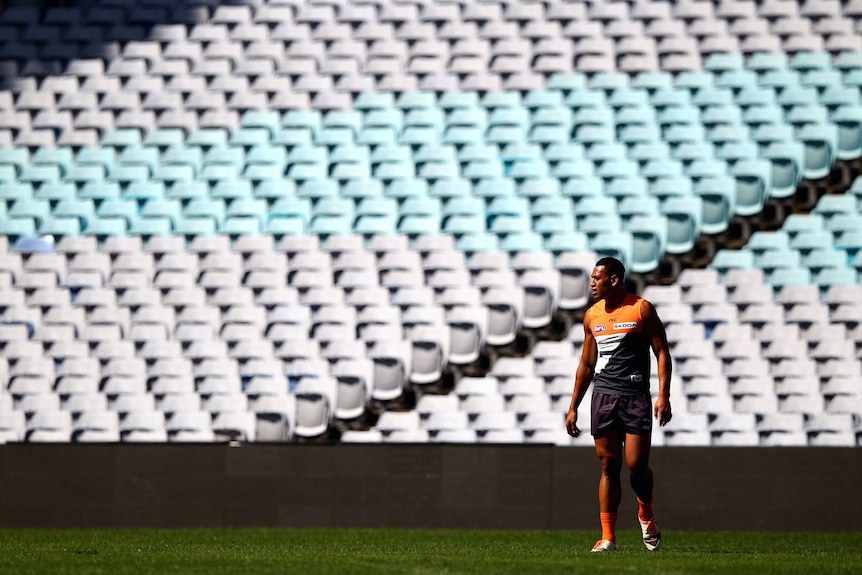 Israel Folau stands in front of an empty stand of pale blue seats wearing a Giants kit