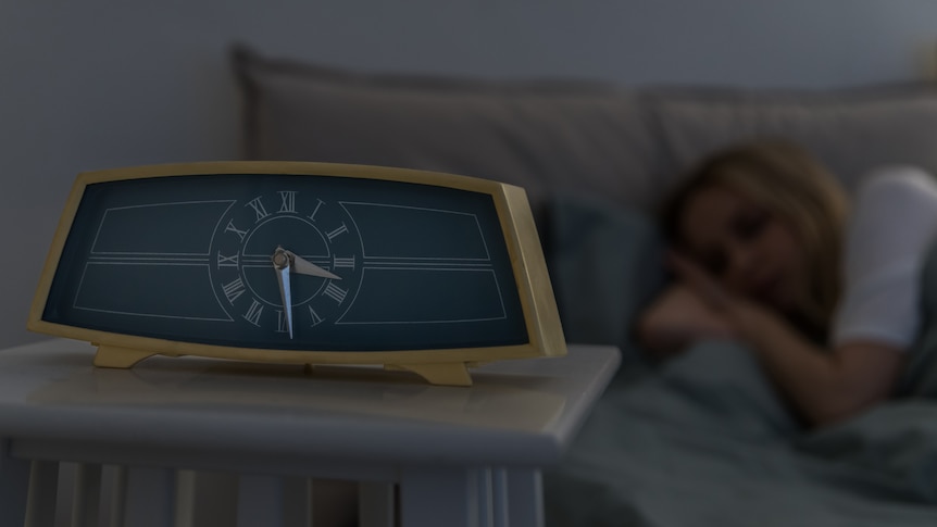 Close up of clock on table with woman sleeping in background