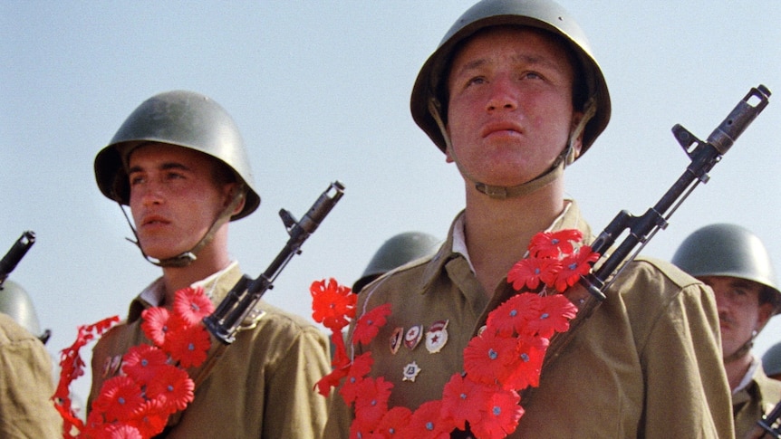 Red Army soldiers wearing paper garlands holding their AK-74 Kalashnikov assault rifles and bouquets of red carnations