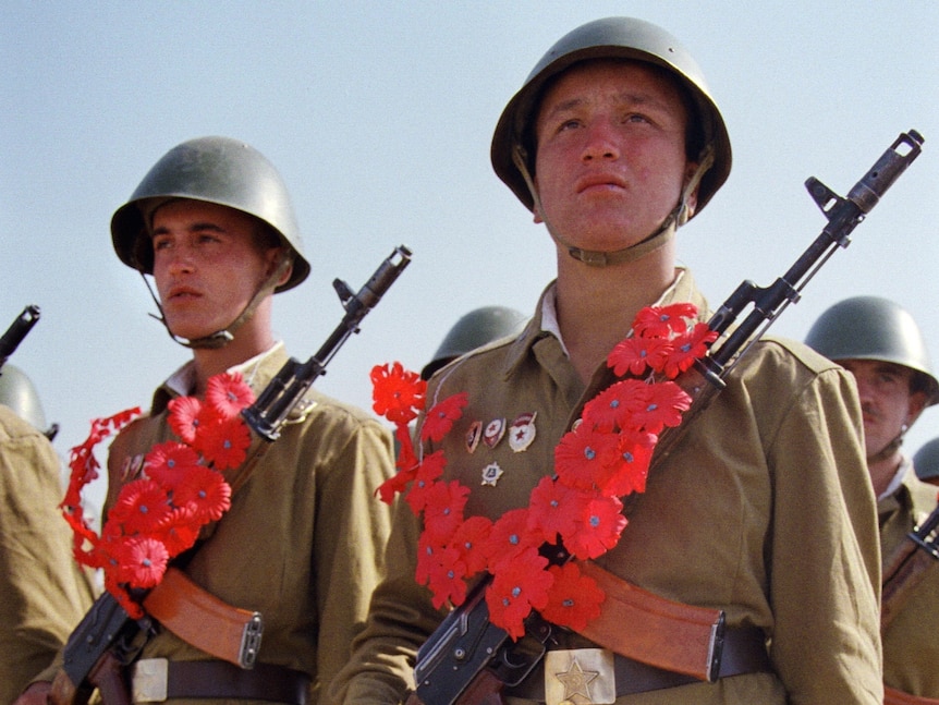 Red Army soldiers wearing paper garlands holding their AK-74 Kalashnikov assault rifles and bouquets of red carnations