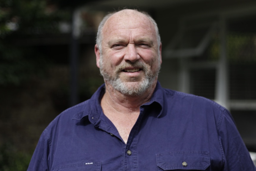 A man with a balding head and grey beard smiles at the camera. 