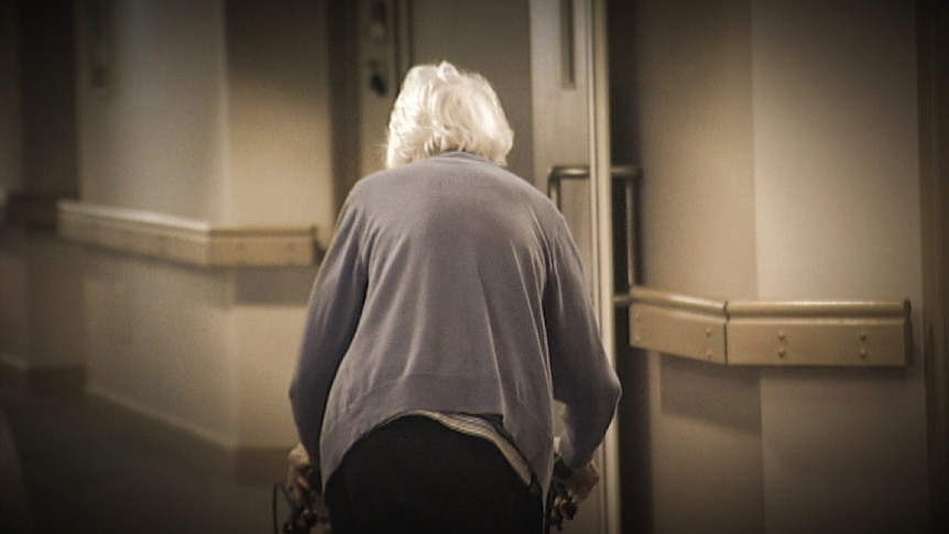 An elderly woman walking with a frame.