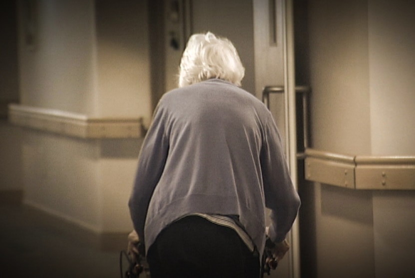 An elderly woman walking with a frame.