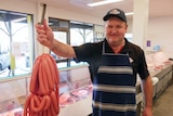 Butcher holds a large string of sausages smiling