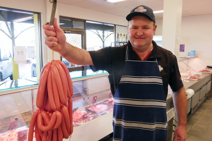 Butcher holds a large string of sausages smiling