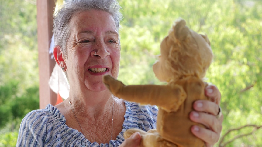 Woman looking at an old teddy bear, smiling fondly
