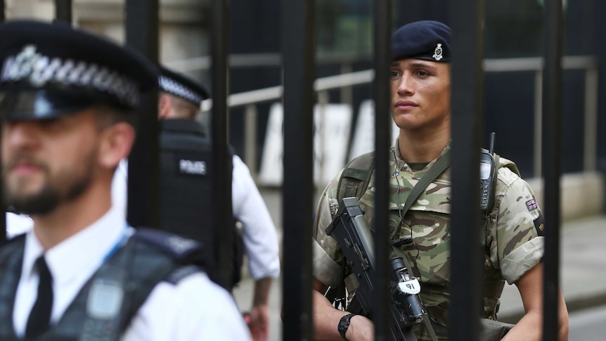 A soldier stands behind the railings as a police officer stands in front in Downing Street in London.
