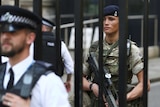 A soldier stands behind the railings as a police officer stands in front in Downing Street in London.