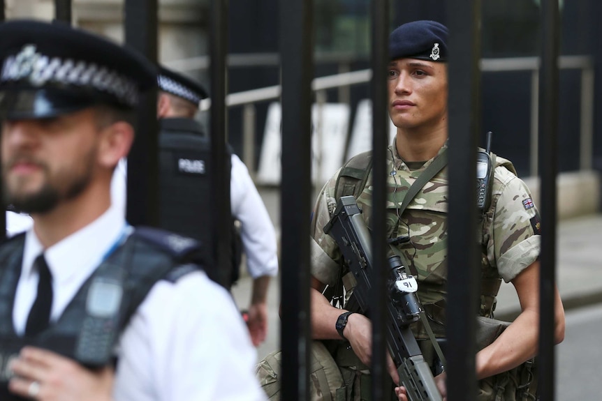 A soldier stands behind the railings as a police officer stands in front in Downing Street in London.