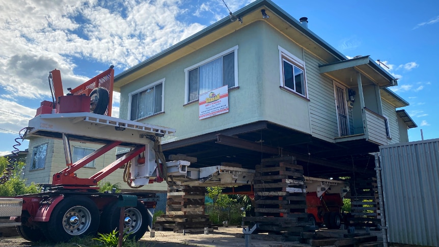 A green house being raised with a truck and wooden stacks underneath.