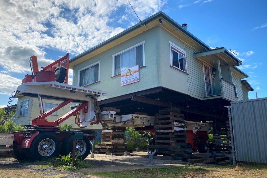 A green house being raised with a truck and wooden stacks underneath.