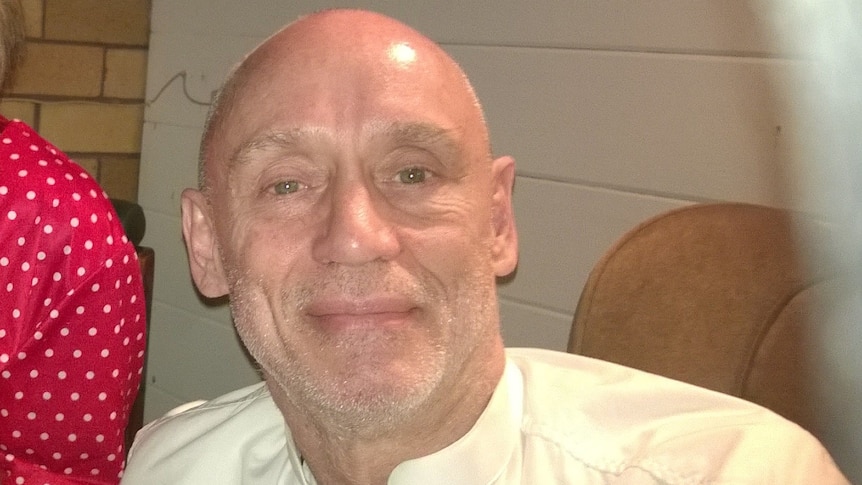 Bald man in white shirt smiles at camera