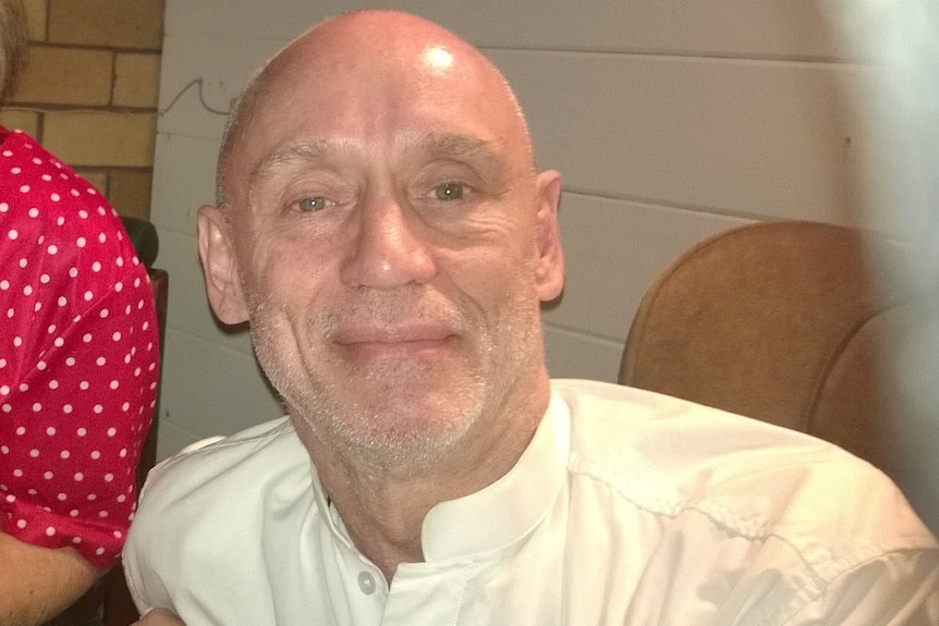 Bald man in white shirt smiles at camera