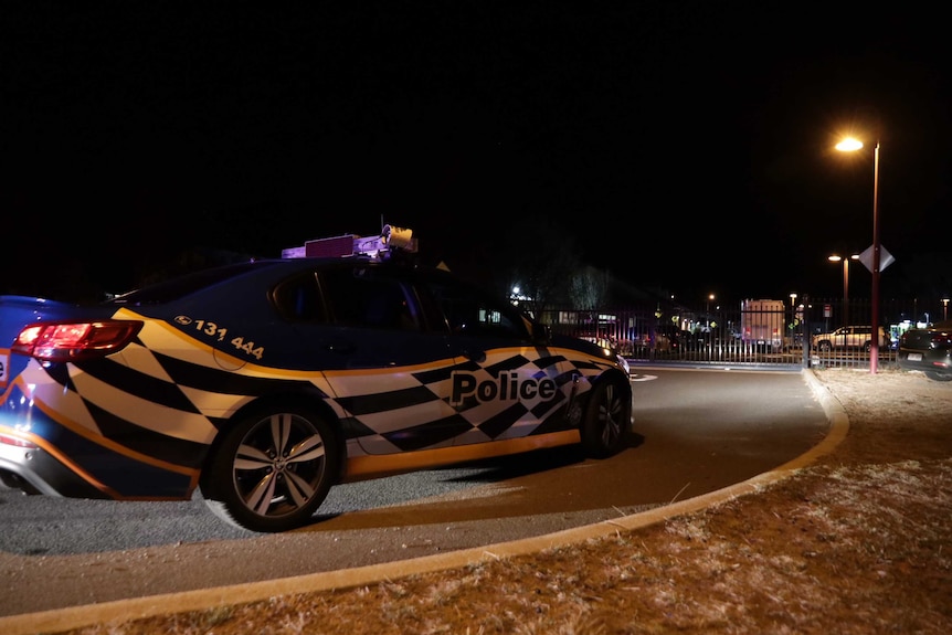 A police car sits outside a metal fence surrounding a primary school car park.