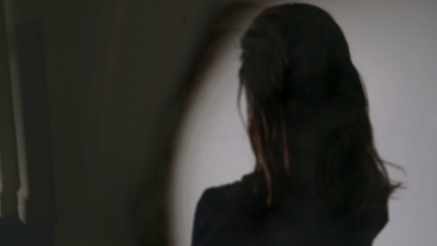 The back of a women looking down a dark hallway in shadows