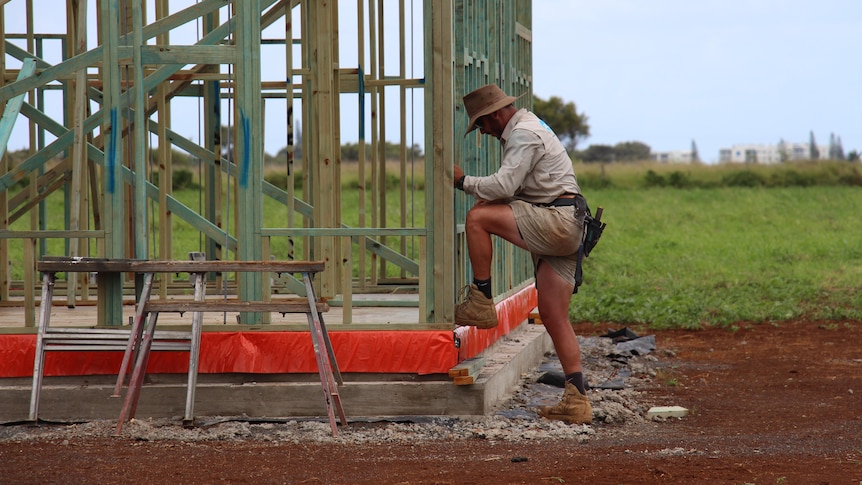 The side of a builder leaning against a timber house frame