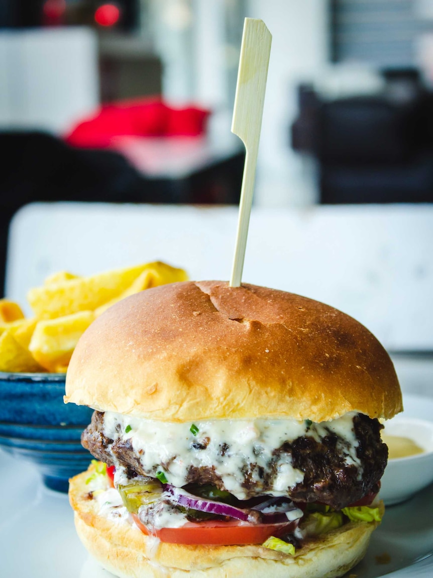A burger and chips sits on a plate, looking delicious.