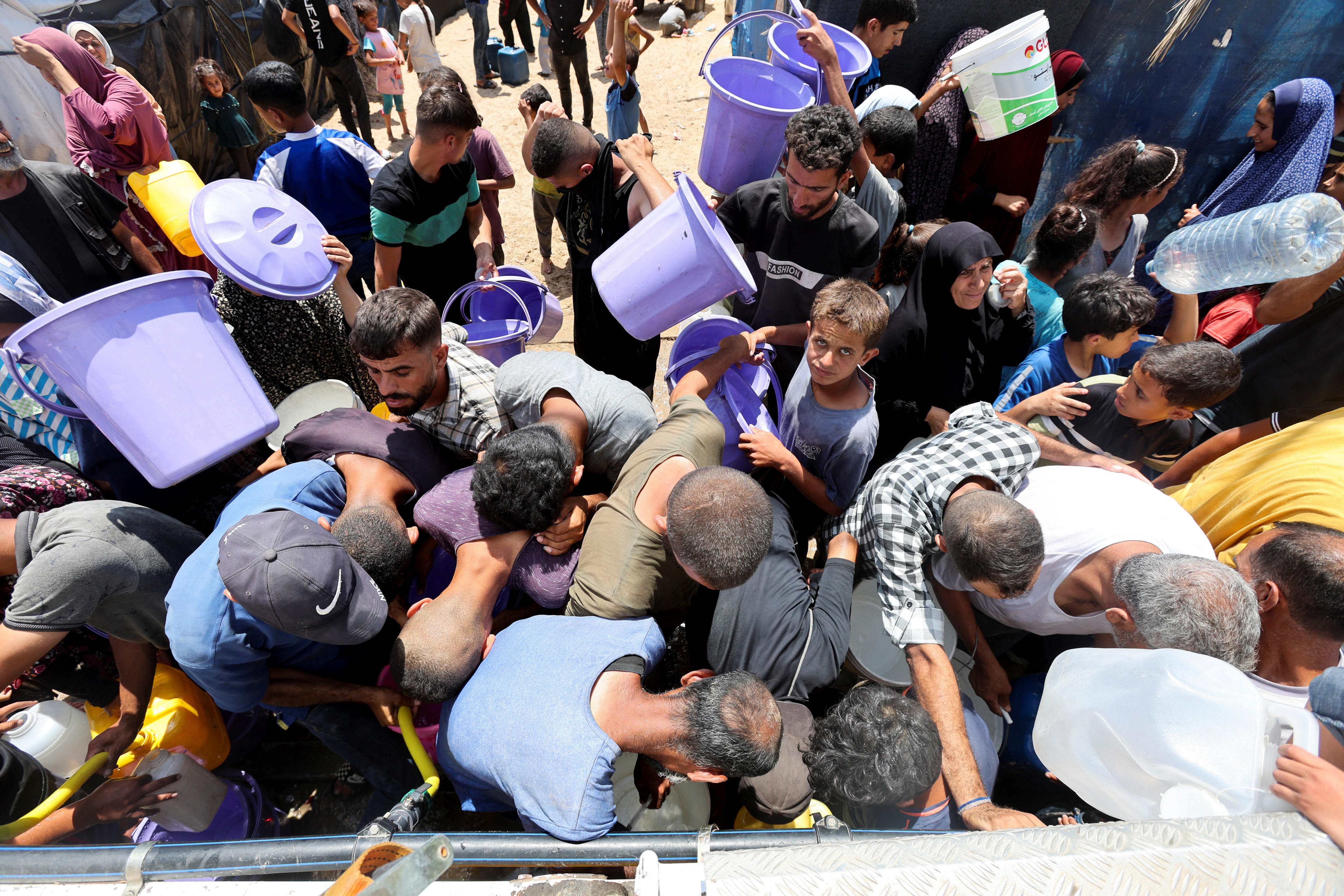 Displaced Palestinians, who fled their house due to Israeli strikes, seek water at a tent camp.