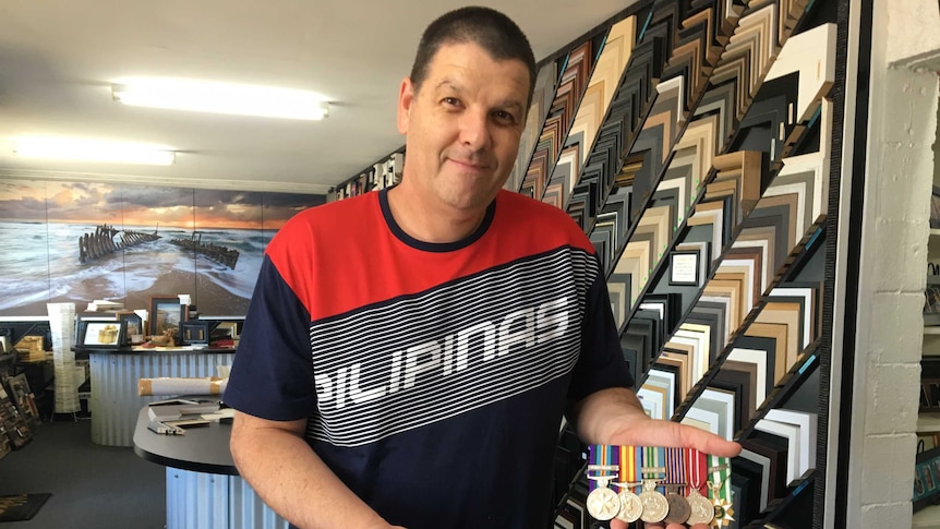 A man holds two sets of replica medals