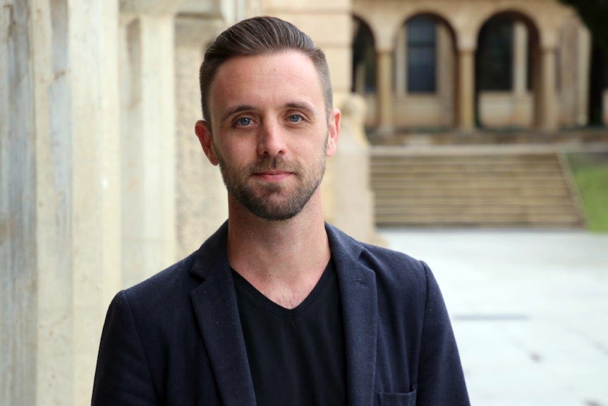 Glenn Savage standing on the UWA campus, with beige coloured buildings in the background.