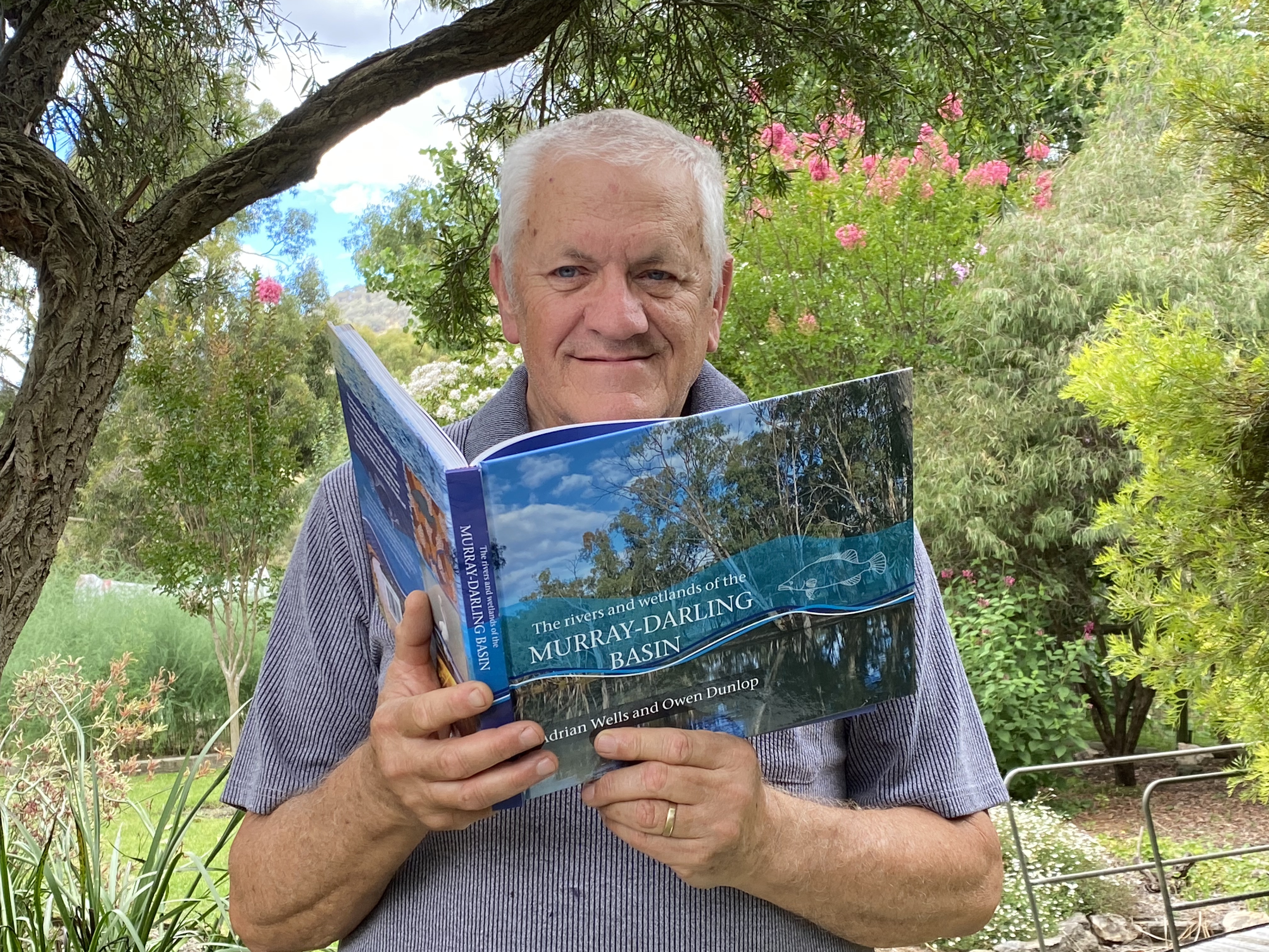 Adrian Wells holds a copy of his book while sitting in a garden.