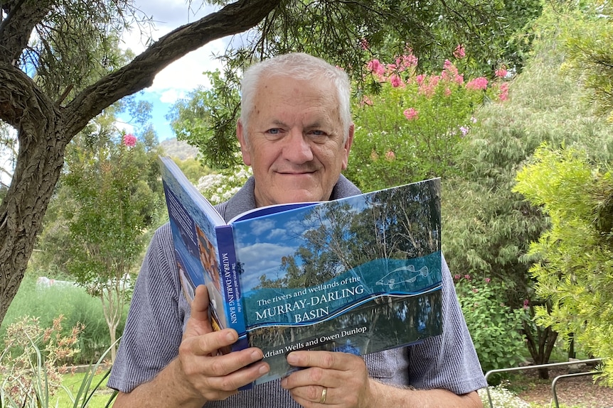 Adrian Wells holds a copy of his book while sitting in a garden.