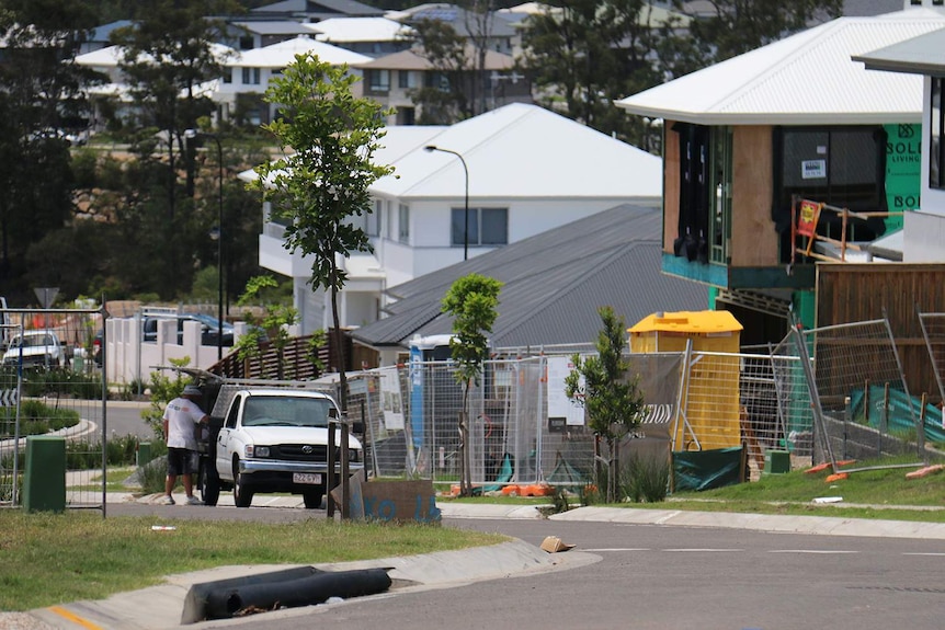 Tradesman stands at trailer outside house construction site at housing estate.