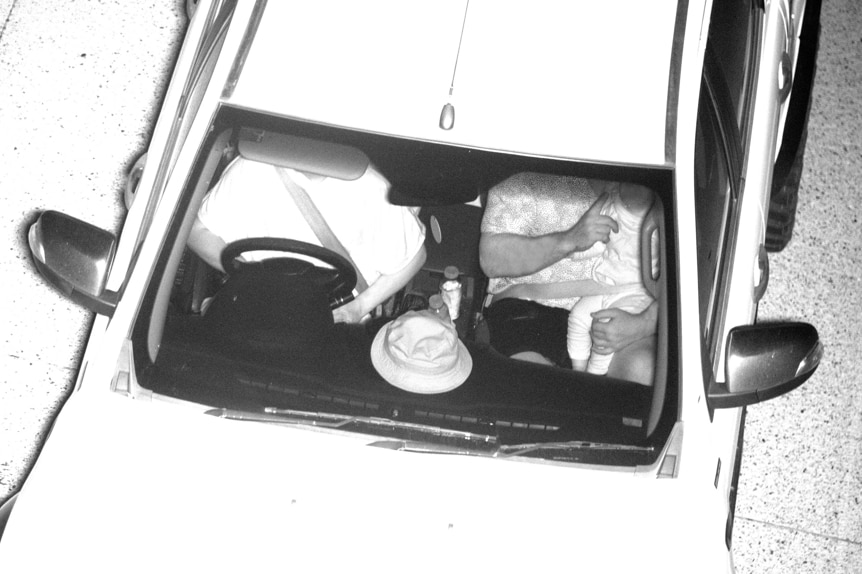 A black and white camera photo of a baby being held by a passenger in a car