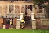 Two firefighters walk towards the stair entrance of an historic looking building damaged by fire
